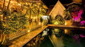 A nighttime view of a hotel courtyard with a stone pathway leading to a reflective pool, surrounded by lush greenery and illuminated by warm lighting. - Simons Heritage Resort Puerto Galera (Puerto Galera)