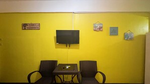 A room with yellow walls, a flat-screen TV mounted on the wall, two wicker chairs, and a small table. There are three framed pictures on the wall. - Simons Heritage Resort Puerto Galera (Puerto Galera)