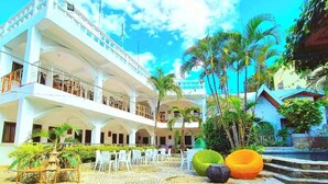 A multi-story hotel with outdoor seating and palm trees. - Simons Heritage Resort Puerto Galera (Puerto Galera)