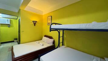 Una habitación con dos literas, una cama individual, una lámpara fijada a la pared y un equipo de aire acondicionado.