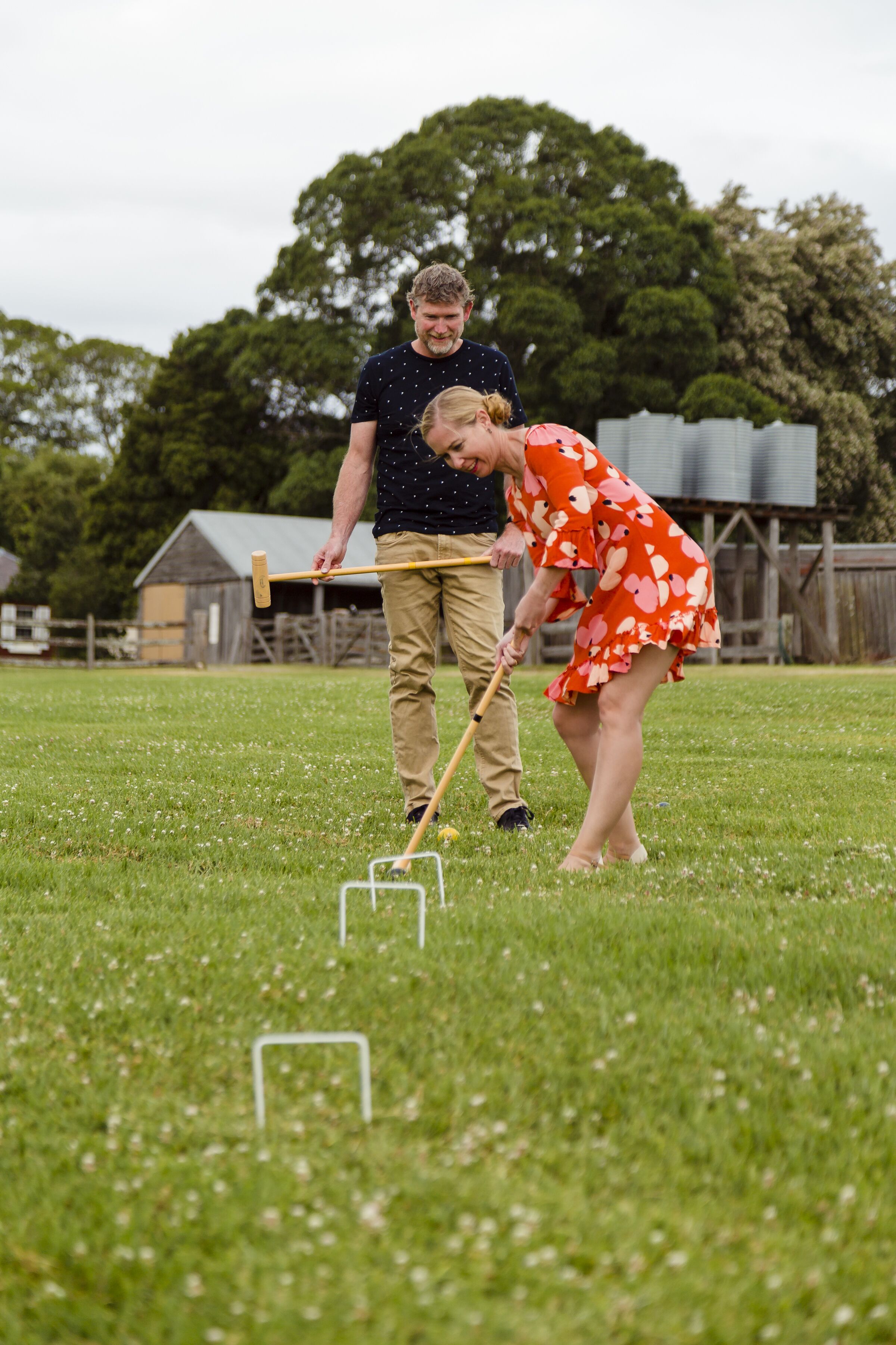Una persona jugando croquet en un campo de césped, con un poste de madera y una pelota.