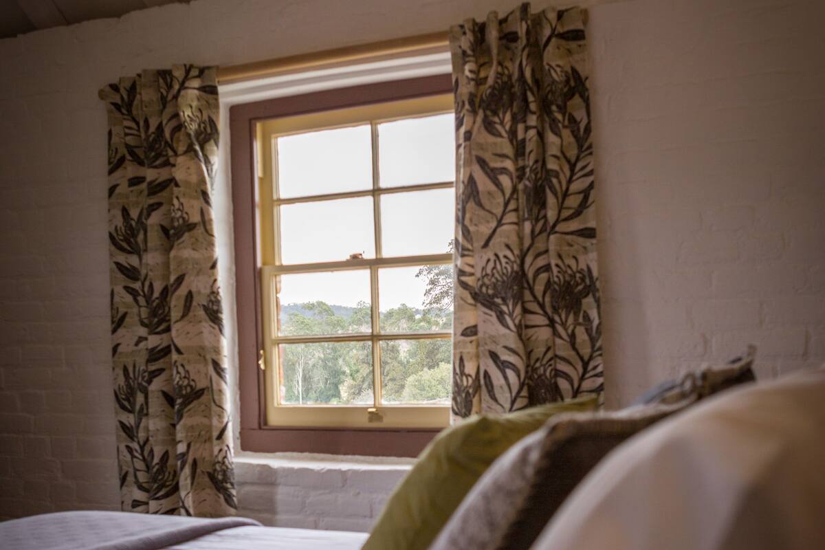 Un dormitorio con un ventanal, una cama con almohadas y vistas a la vegetación exterior.
