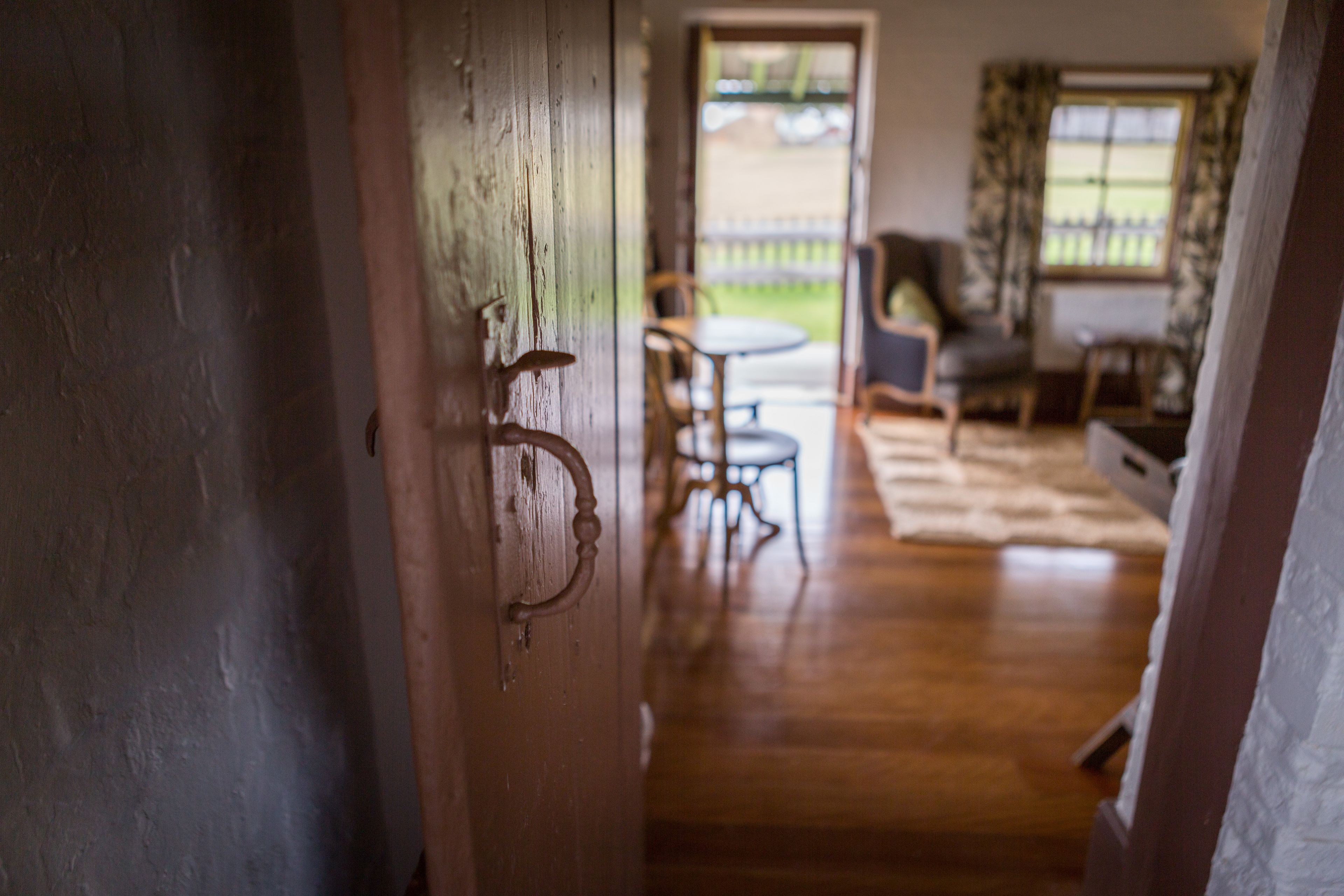 A wooden door leading to a room with a wooden floor, a round table, and a chair.