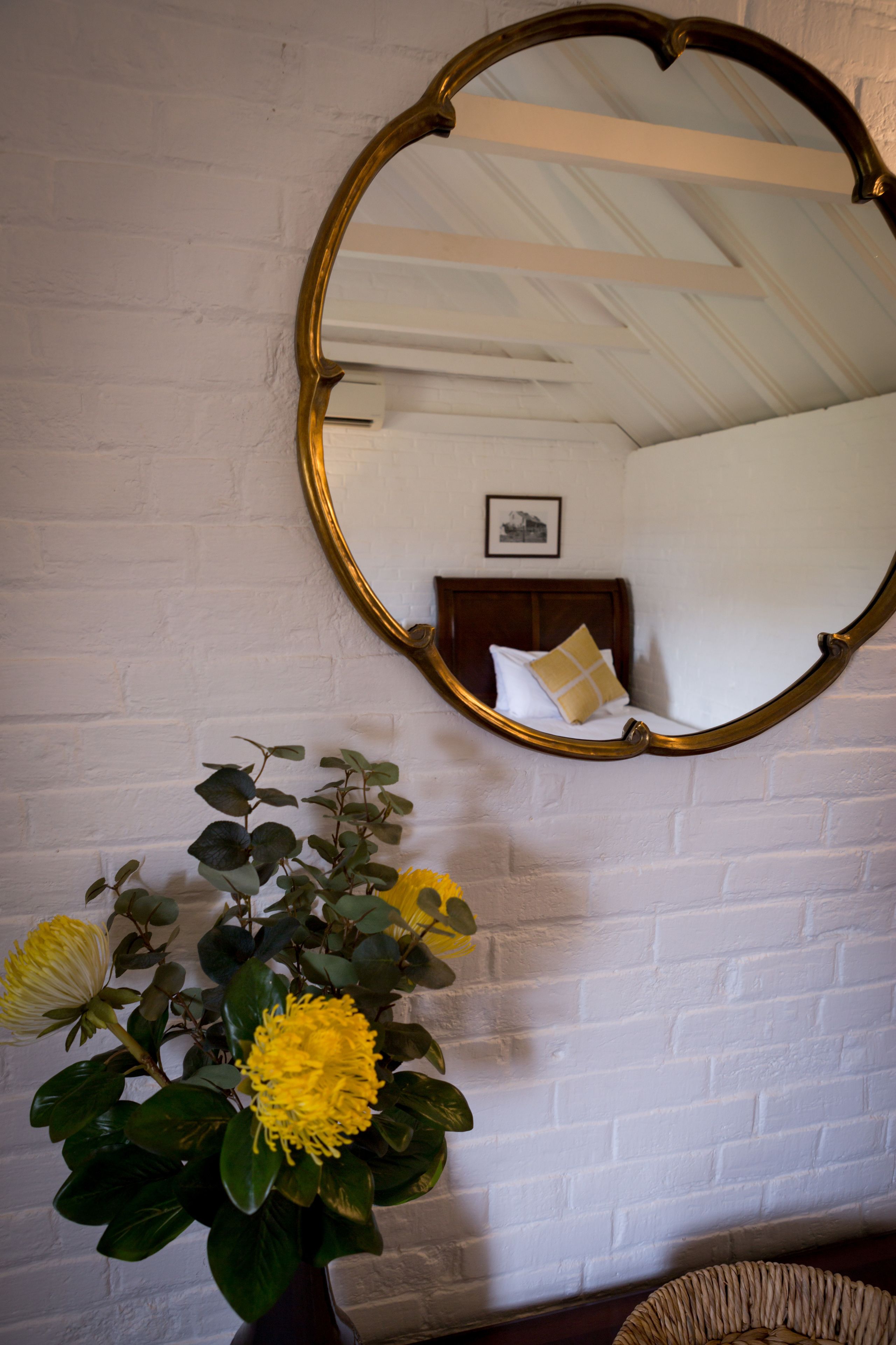 A white brick wall with a round mirror and a vase with yellow flowers.