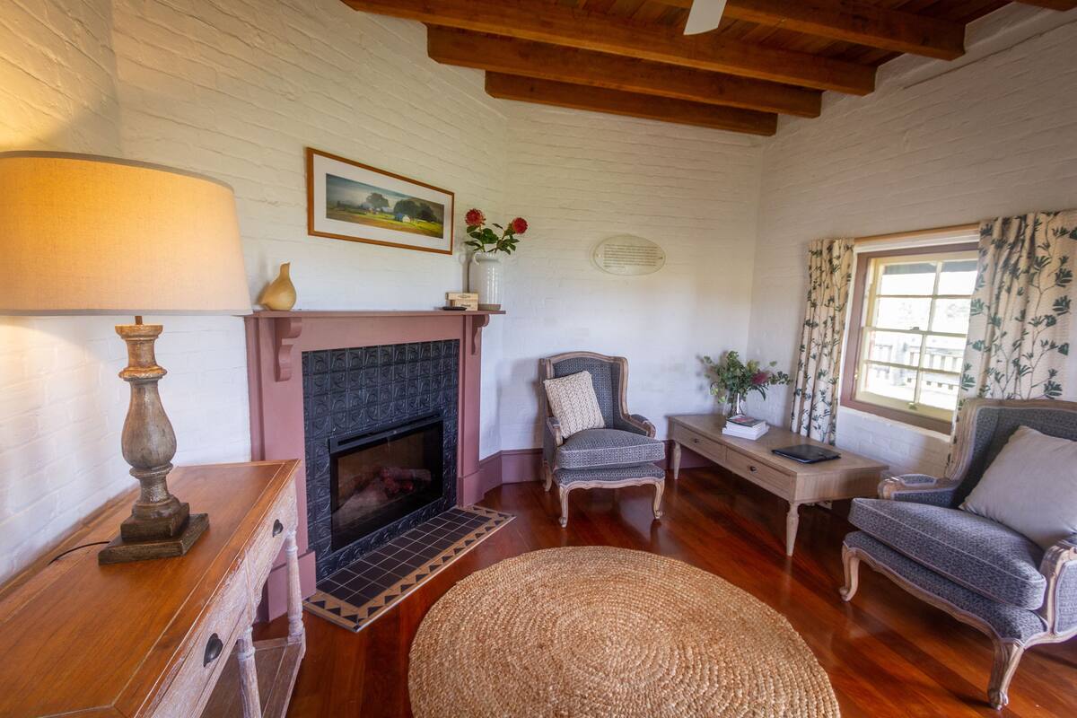 Un salón acogedor con chimenea, muebles de madera y vistas al exterior a través de una ventana con cortinas florales.