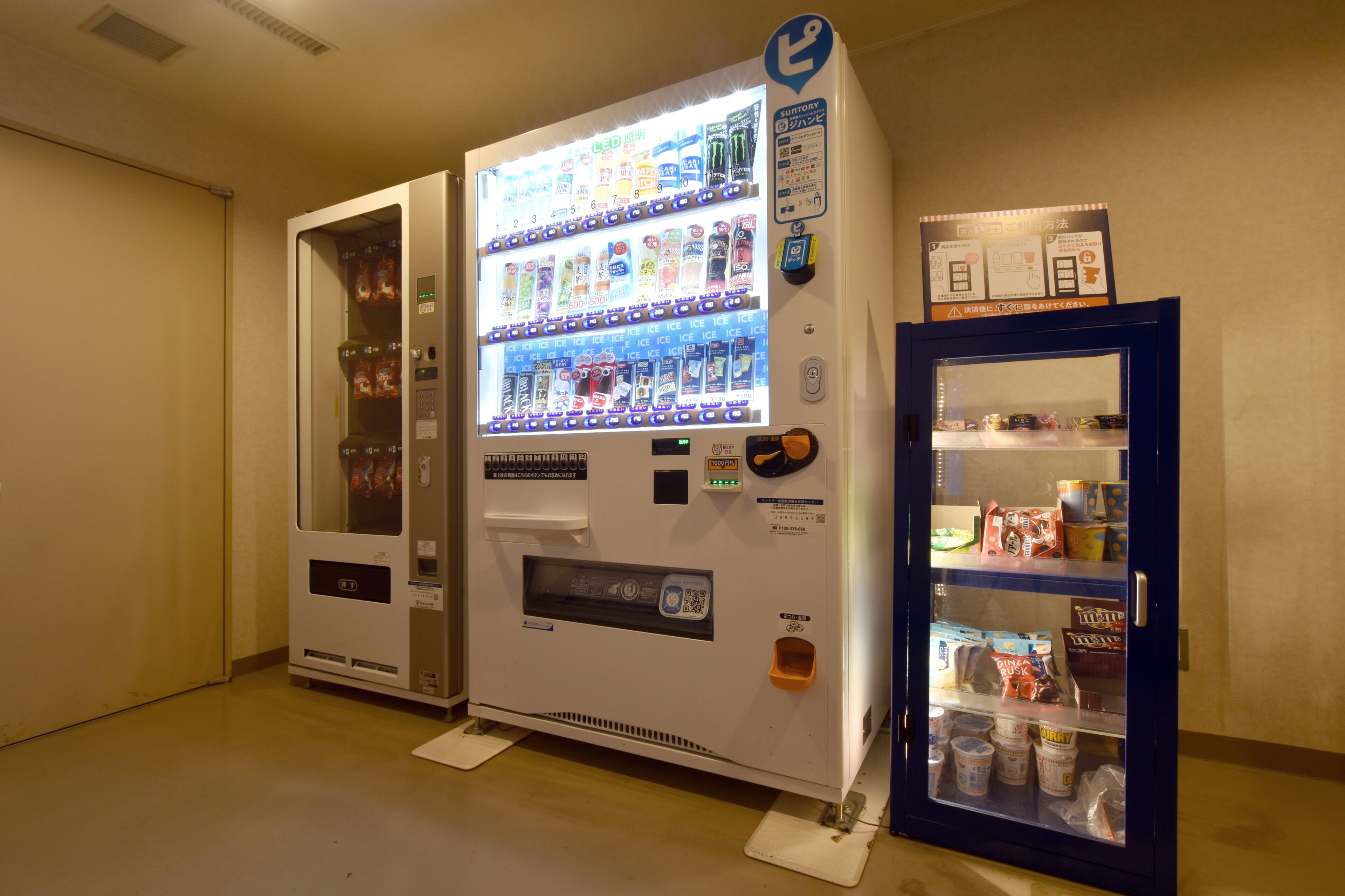 Een automaat met diverse snacks en drankjes, een QR-code en een kleine koelkast met verpakte producten.