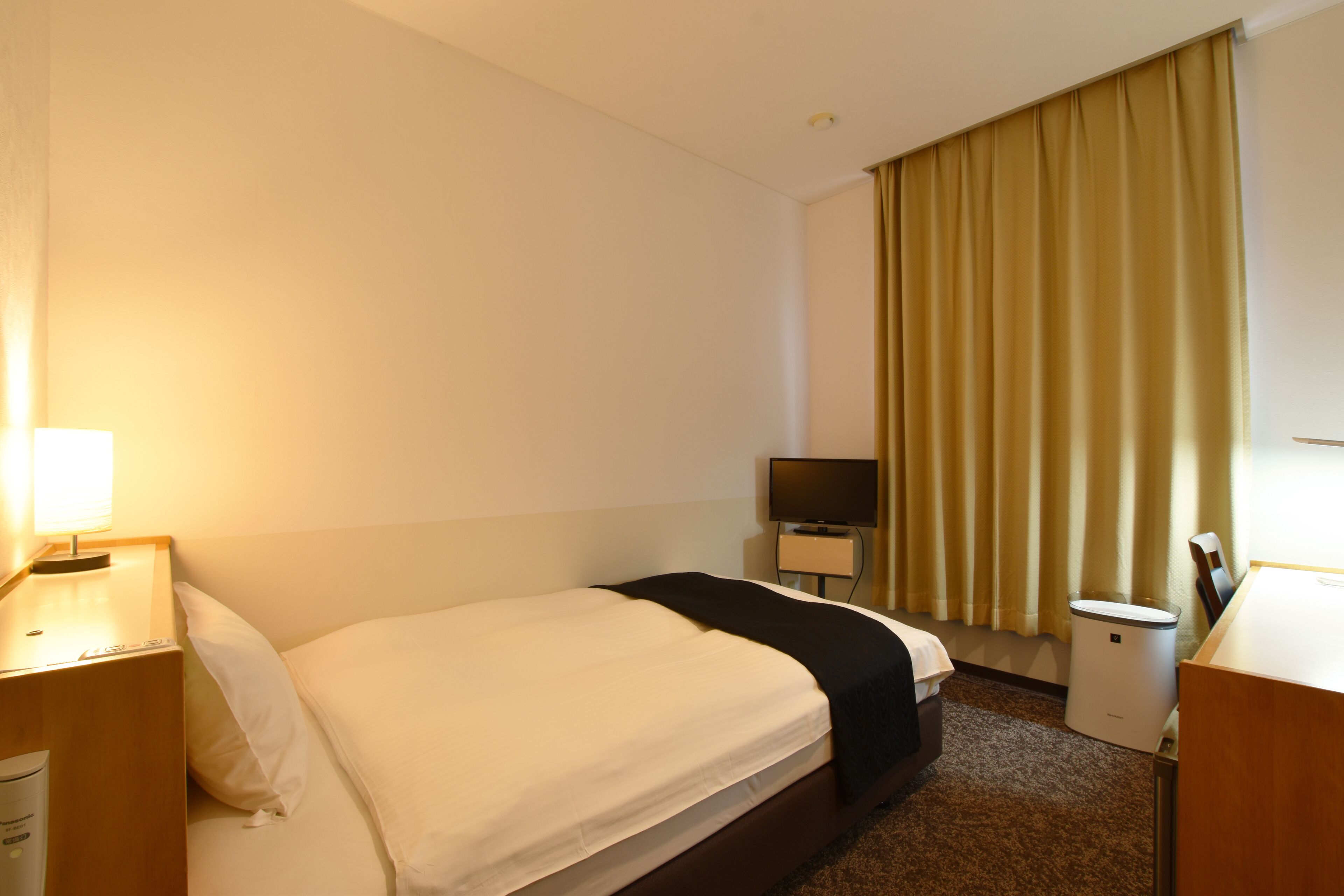 Habitación de hotel con cama, escritorio, televisor y cesto de basura.