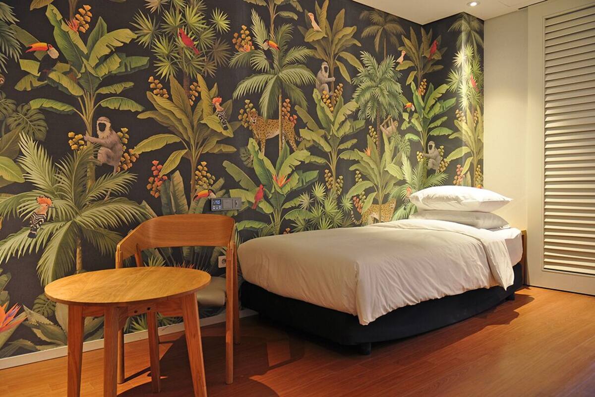 A bedroom with a bed, a chair, and a wall mural of a jungle scene.