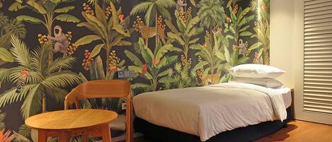 Un dormitorio con una cama, una silla y un mural en la pared que representa una escena de selva.