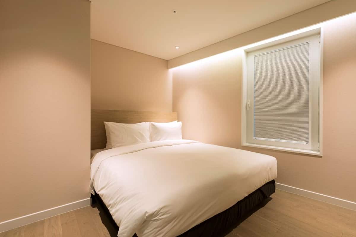 A bedroom with a bed, a window with blinds, and a ceiling light.