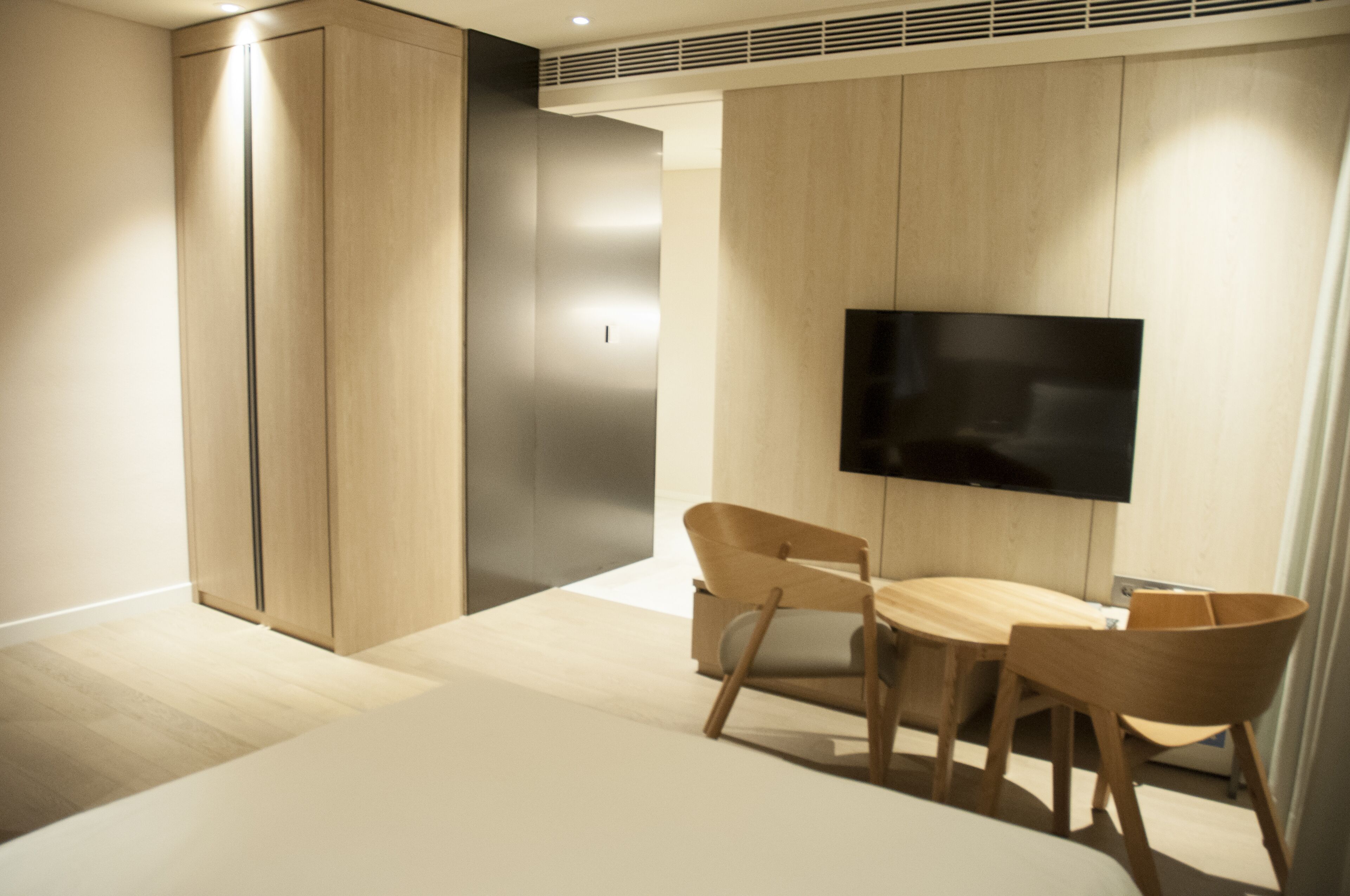 A modern room with a flat-screen TV mounted on the wall, a wooden dining table with chairs, and built-in wooden cabinets.