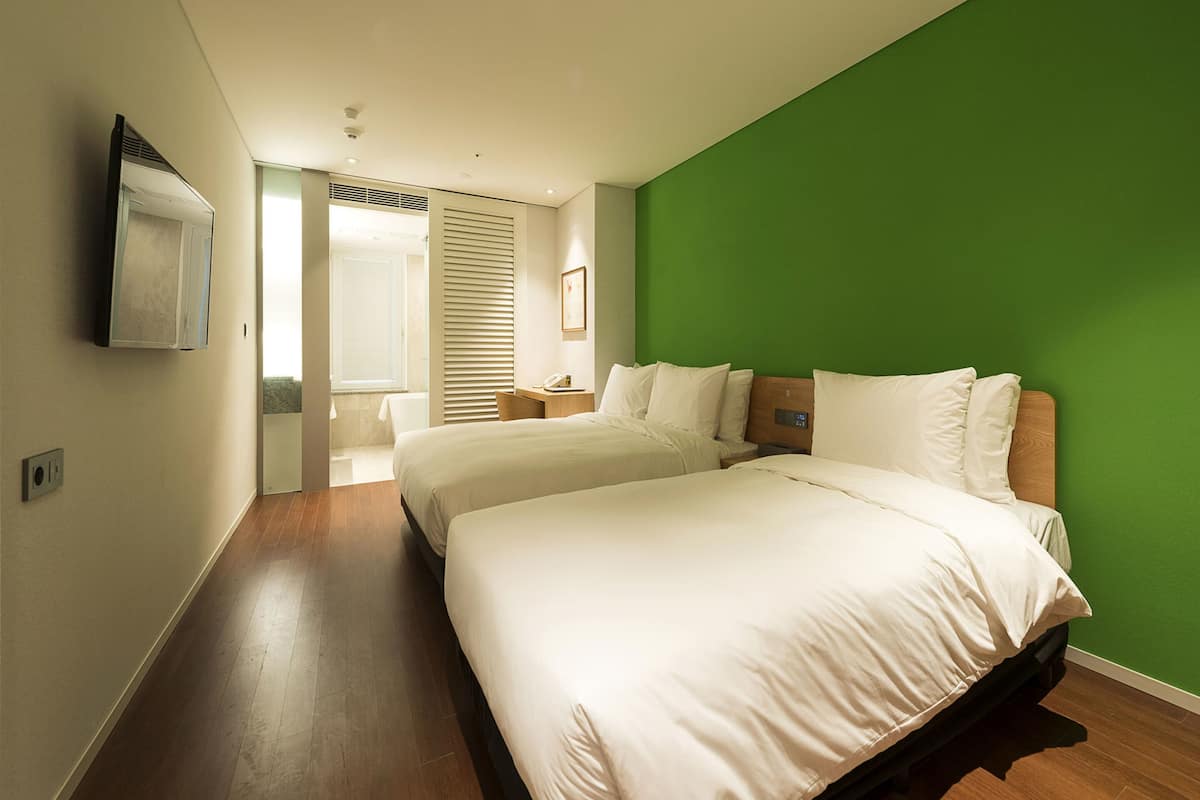 A hotel room with two beds, a green accent wall, and a wooden floor.
