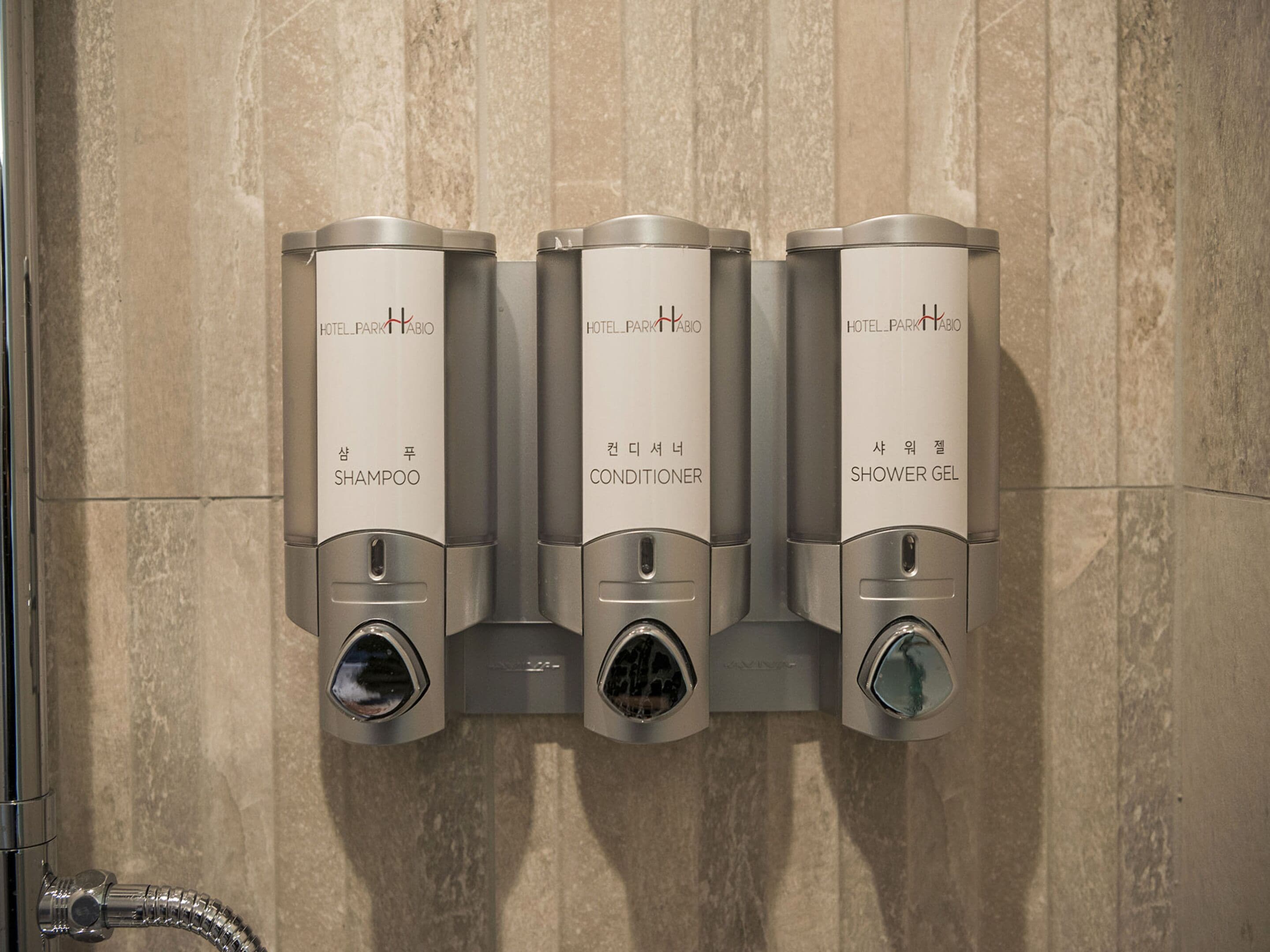 Dispensador empotrado en la pared con tres compartimentos etiquetados para champú, acondicionador y gel de ducha.