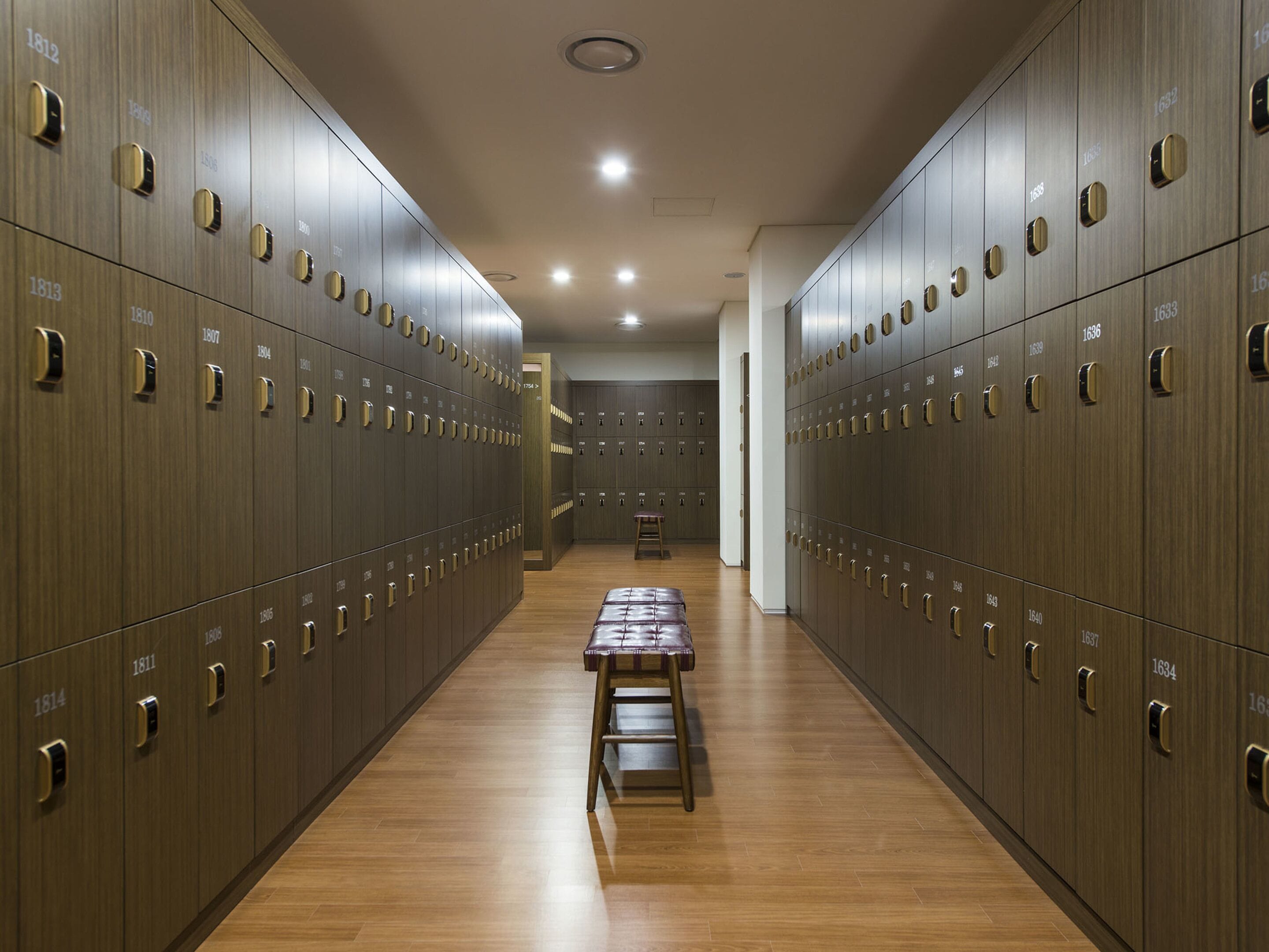 A row of wooden lockers with numbers, a bench, and a wooden floor.