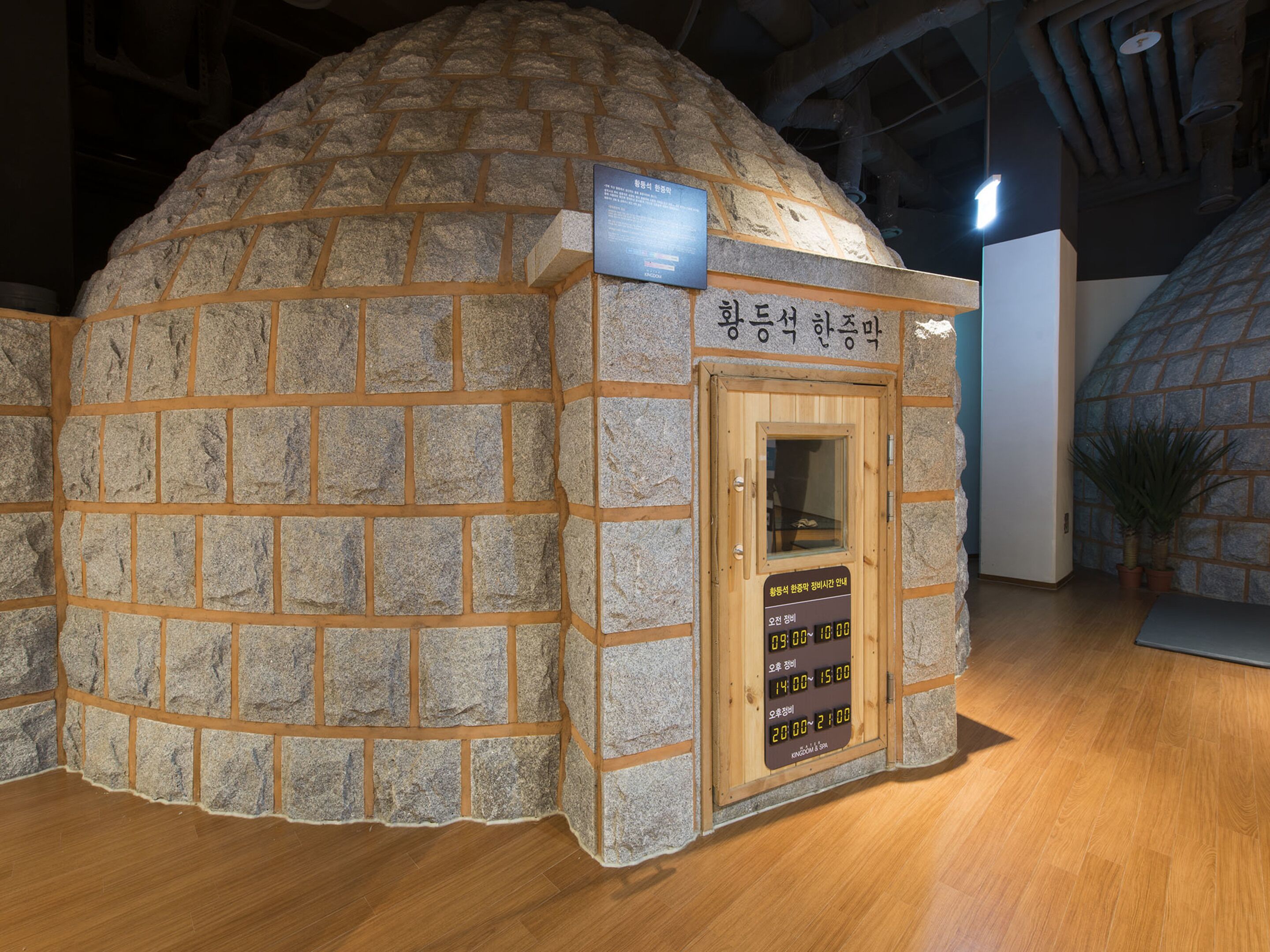 A stone igloo-like structure with a wooden door and a signboard displaying operating hours.