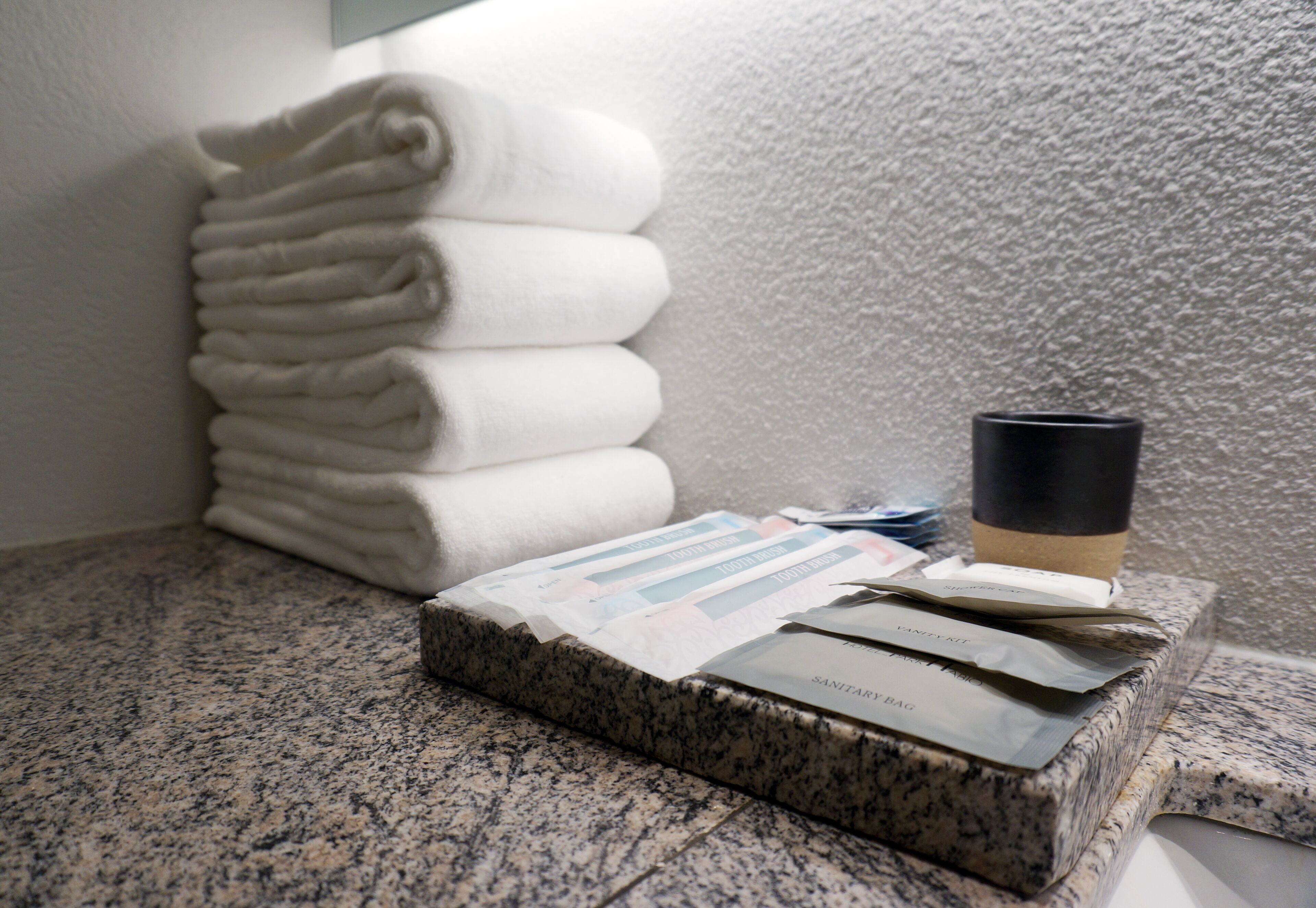 A stack of white towels, a coffee cup, and some magazines on a granite countertop.