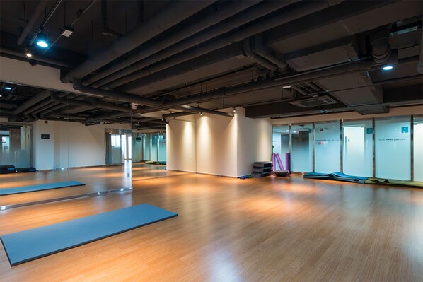 Une salle de sport spacieuse, dotée de planchers en bois, de tapis de sol et d’un plafond haut avec des tuyaux apparents.
