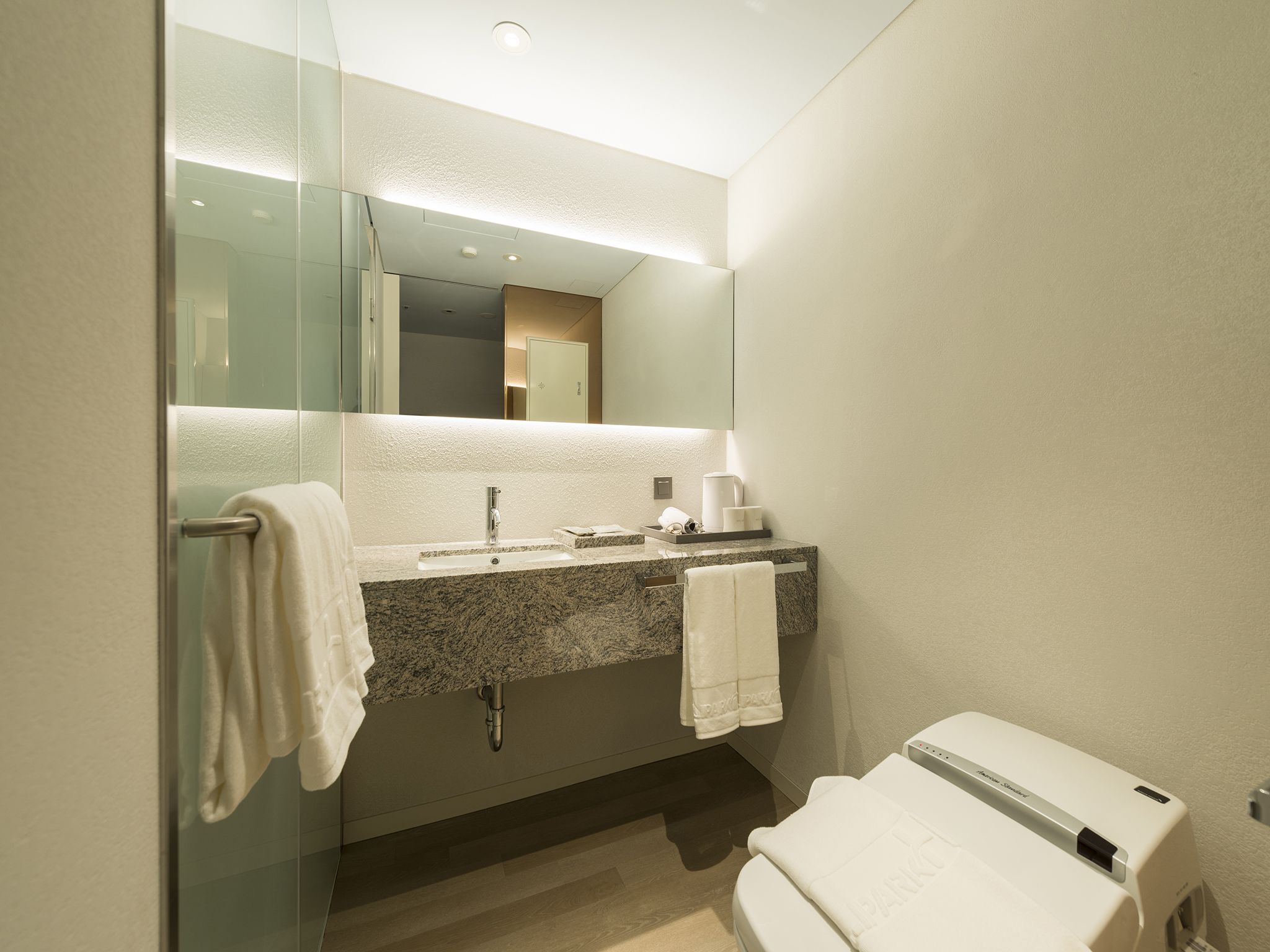 A modern bathroom with a granite countertop sink, a glass shower enclosure, and a white toilet.