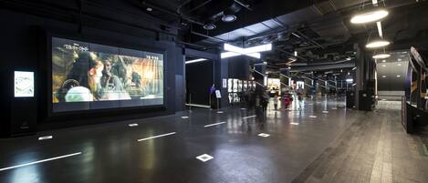 A spacious indoor corridor with a large digital display on the left, a polished floor, and a modern ceiling with lighting fixtures.