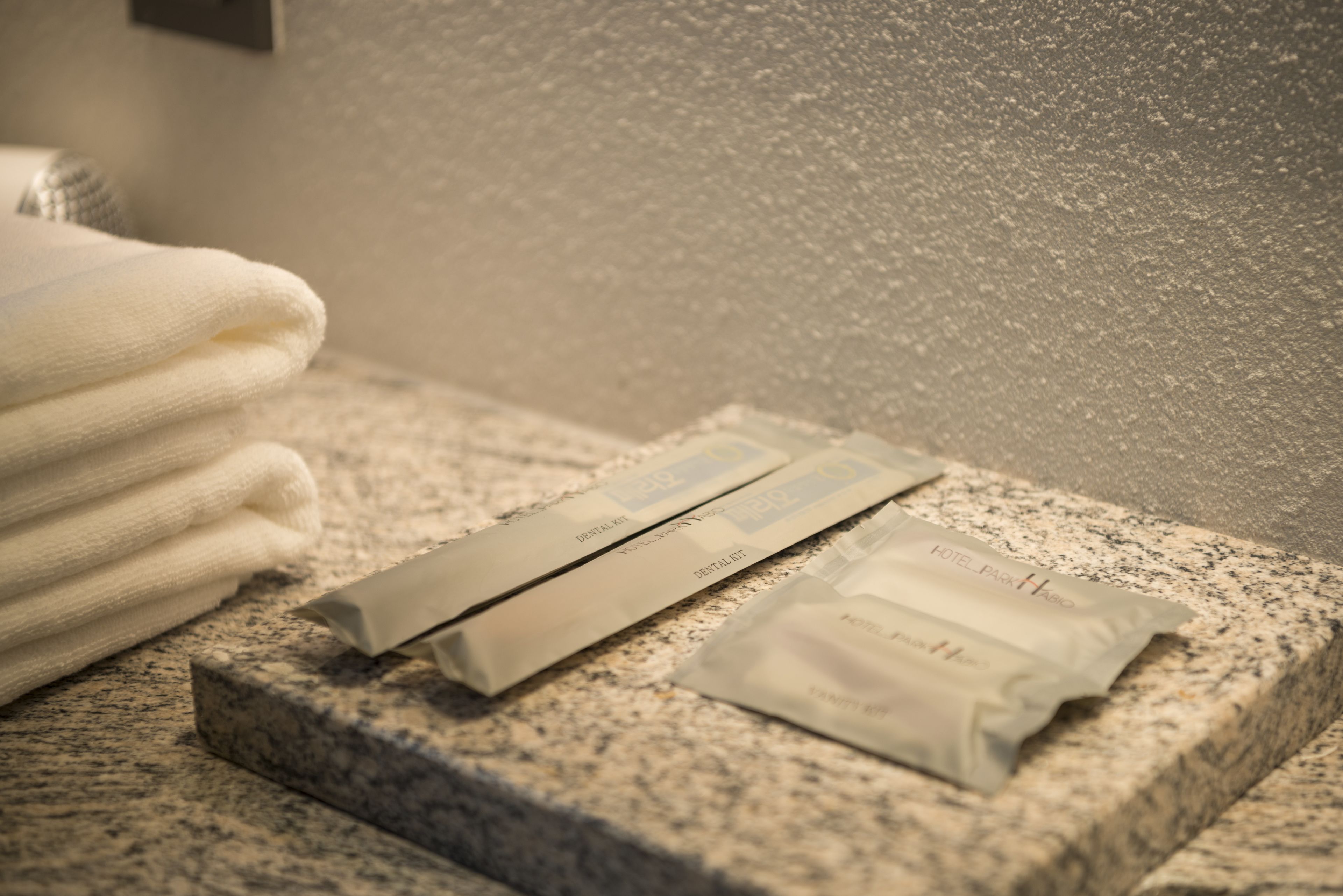 A bathroom with a granite countertop, a folded white towel, and two dental care kits.