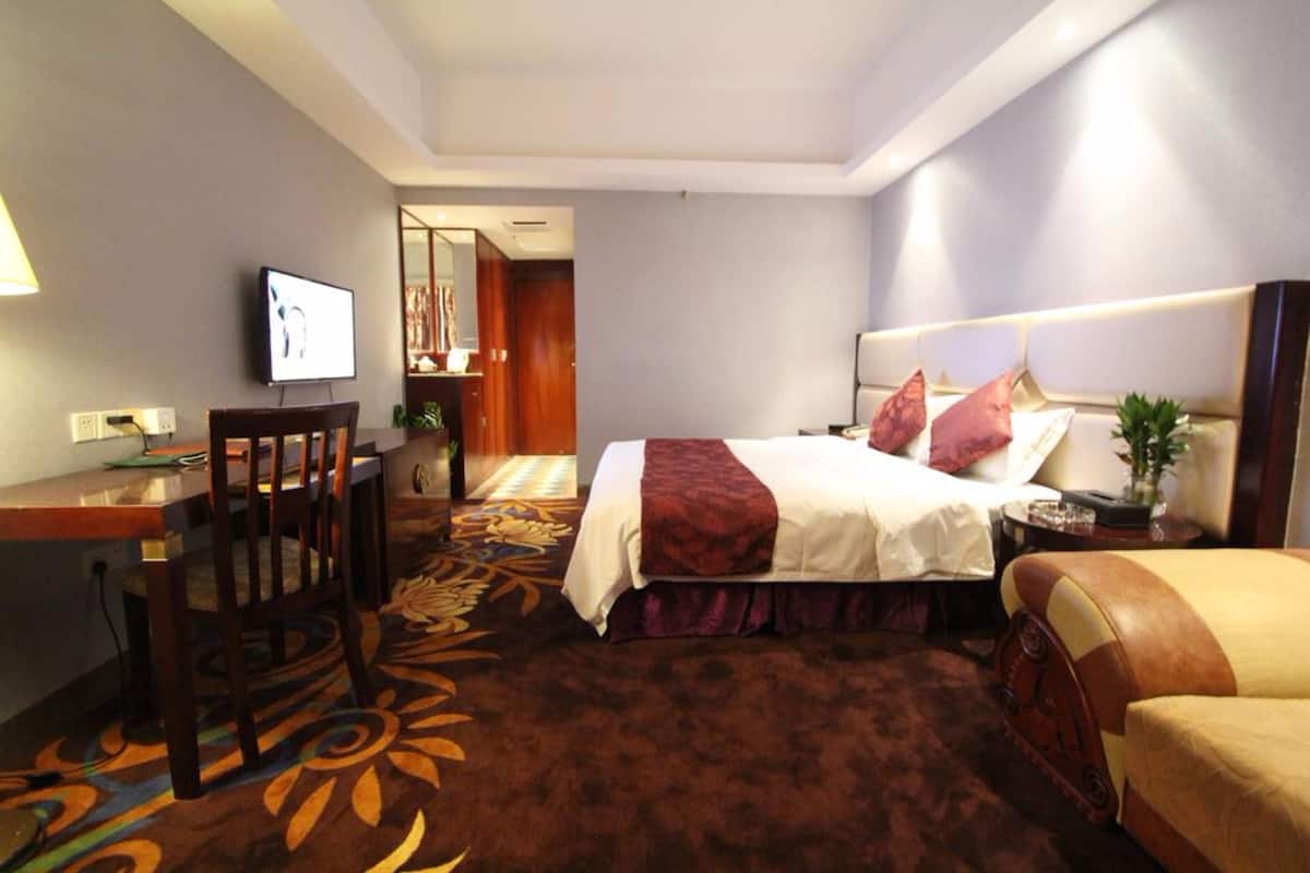 A hotel room with a bed, a desk, a chair, and a TV.