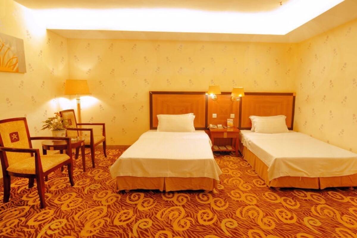 A hotel room with two single beds, a desk with a chair, a lamp, and a patterned carpet.