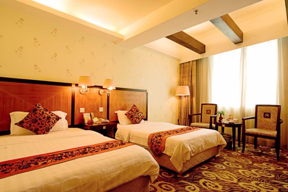 A hotel room with two beds, a wooden headboard, a small table with a lamp, and a chair.