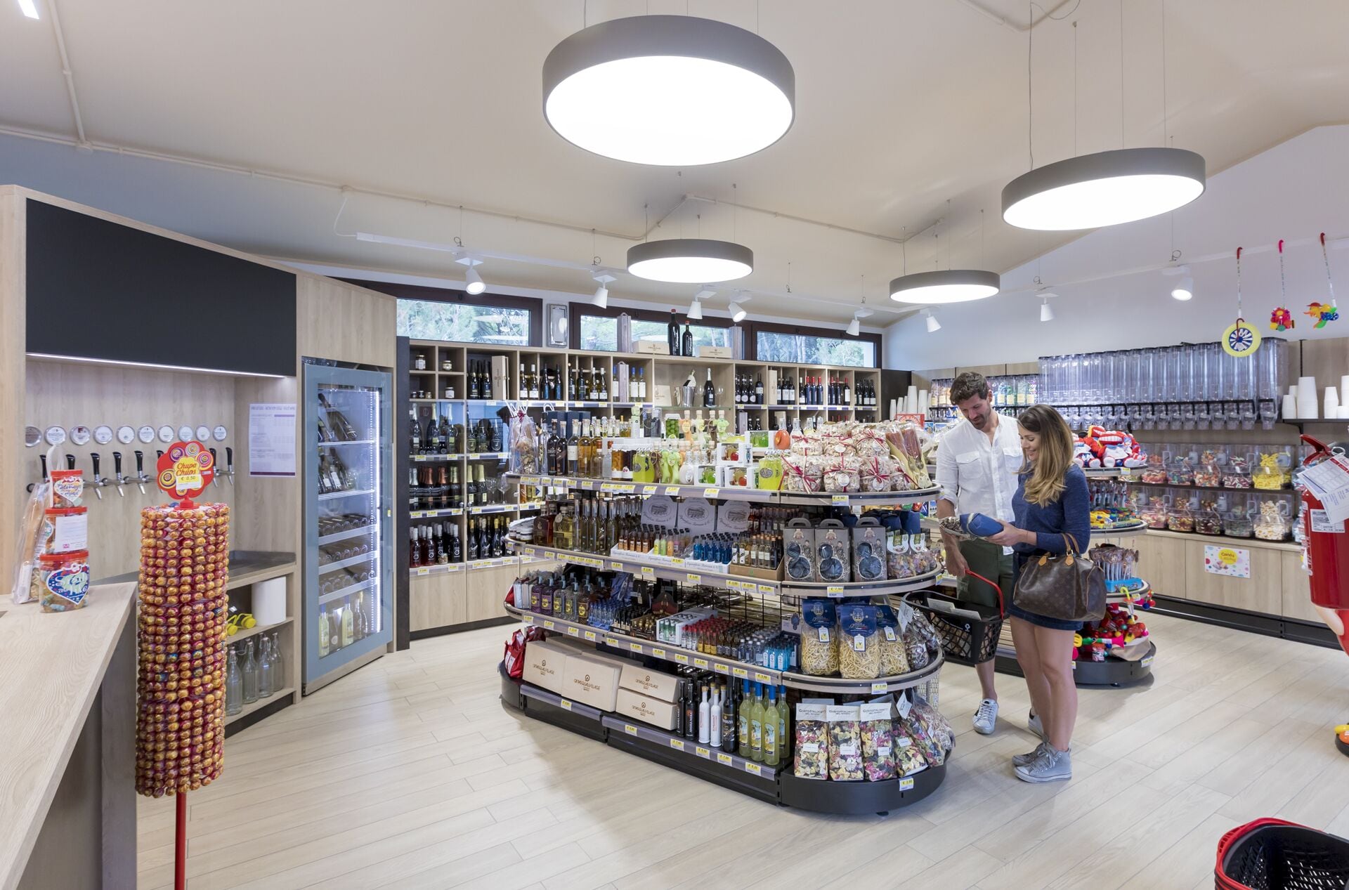 Innenansicht eines Supermarktes mit Regalen voller verschiedener Waren, einer Kühlvitrine und einer Kasse.