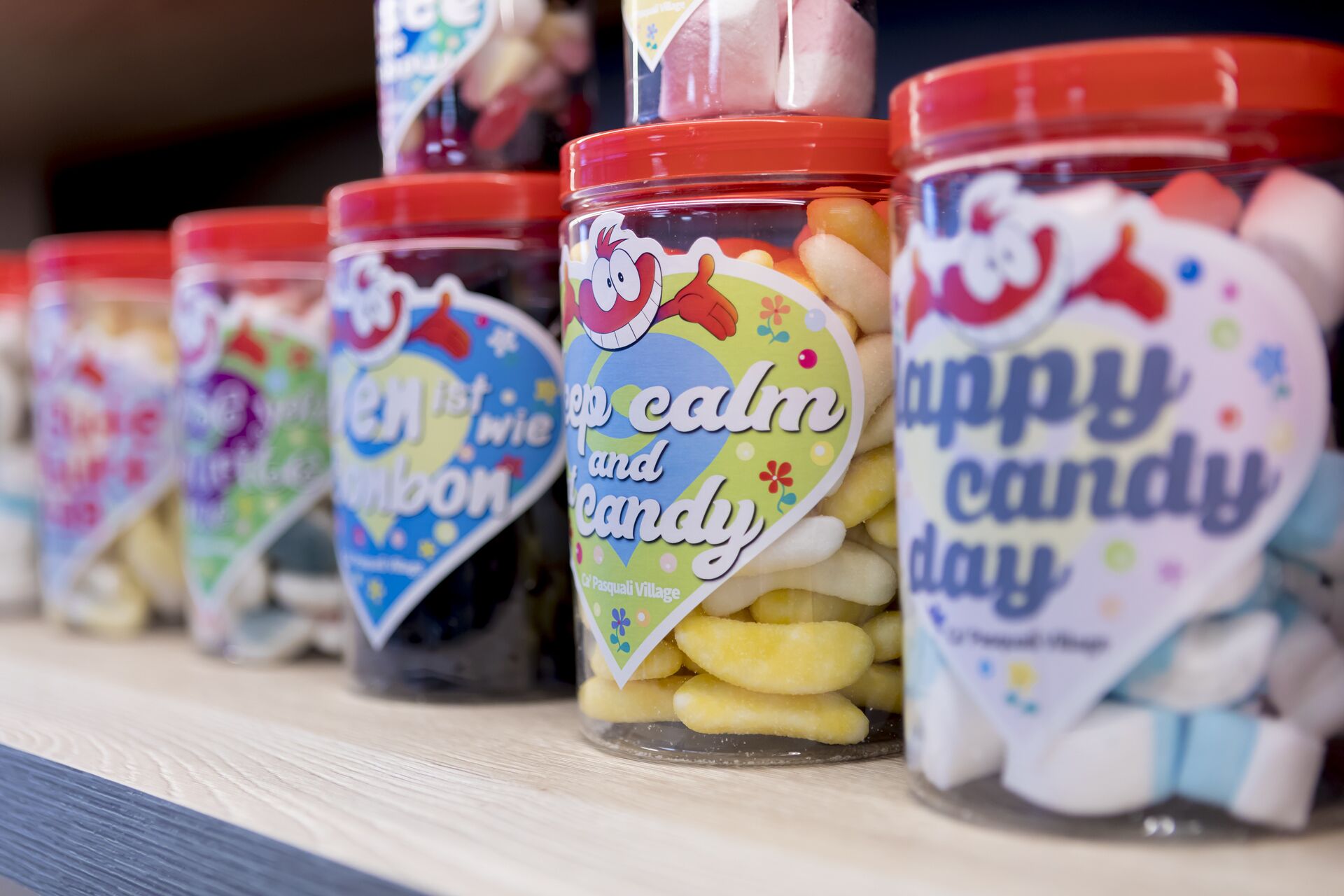 A row of jars with colorful labels, each containing different types of candies.