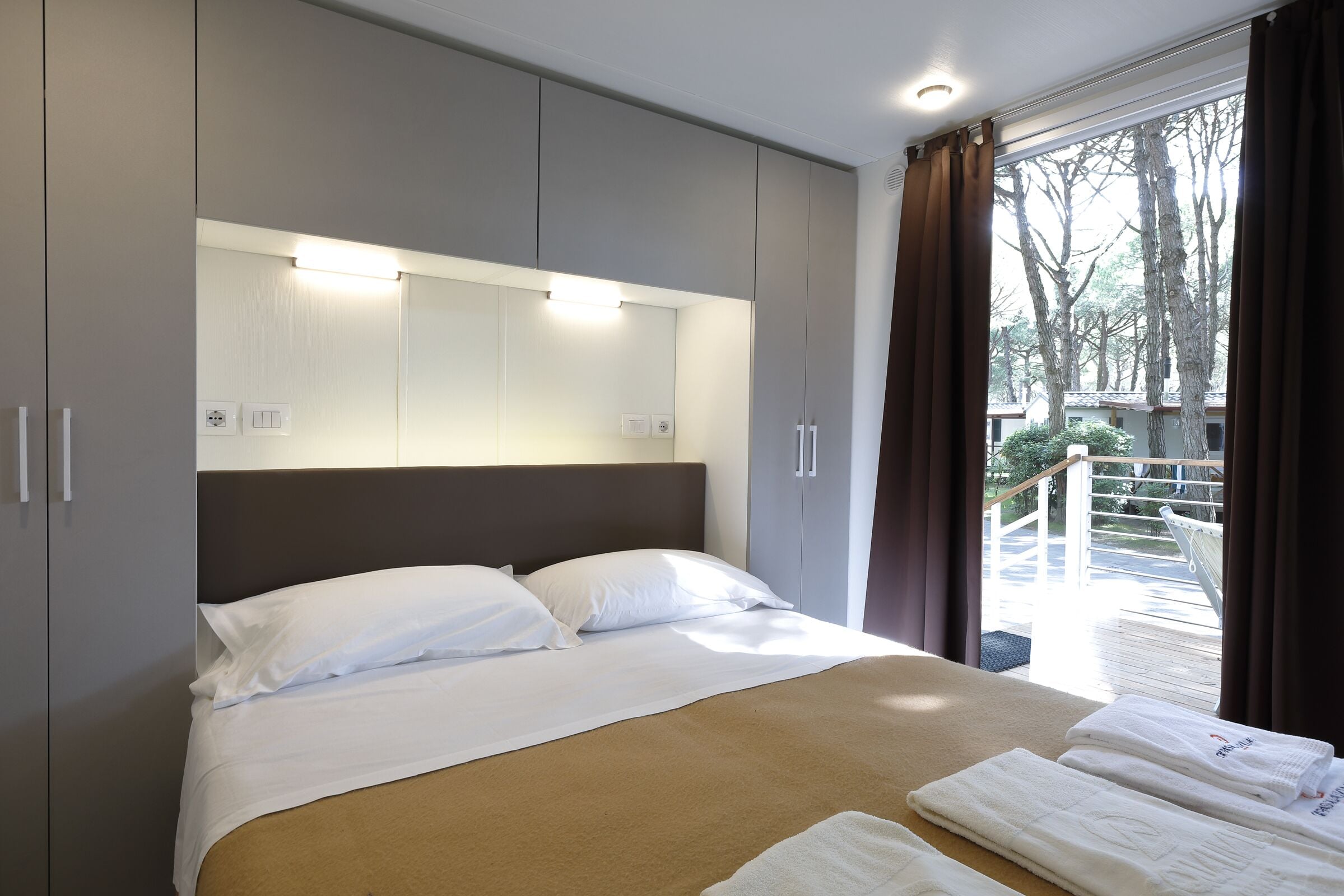 Habitación de hotel moderna con una cama grande, armario gris y vistas al exterior.