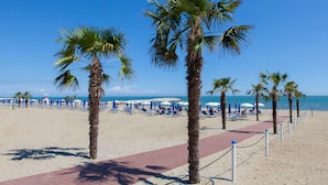 A beach with palm trees, blue lounge chairs, and umbrellas.