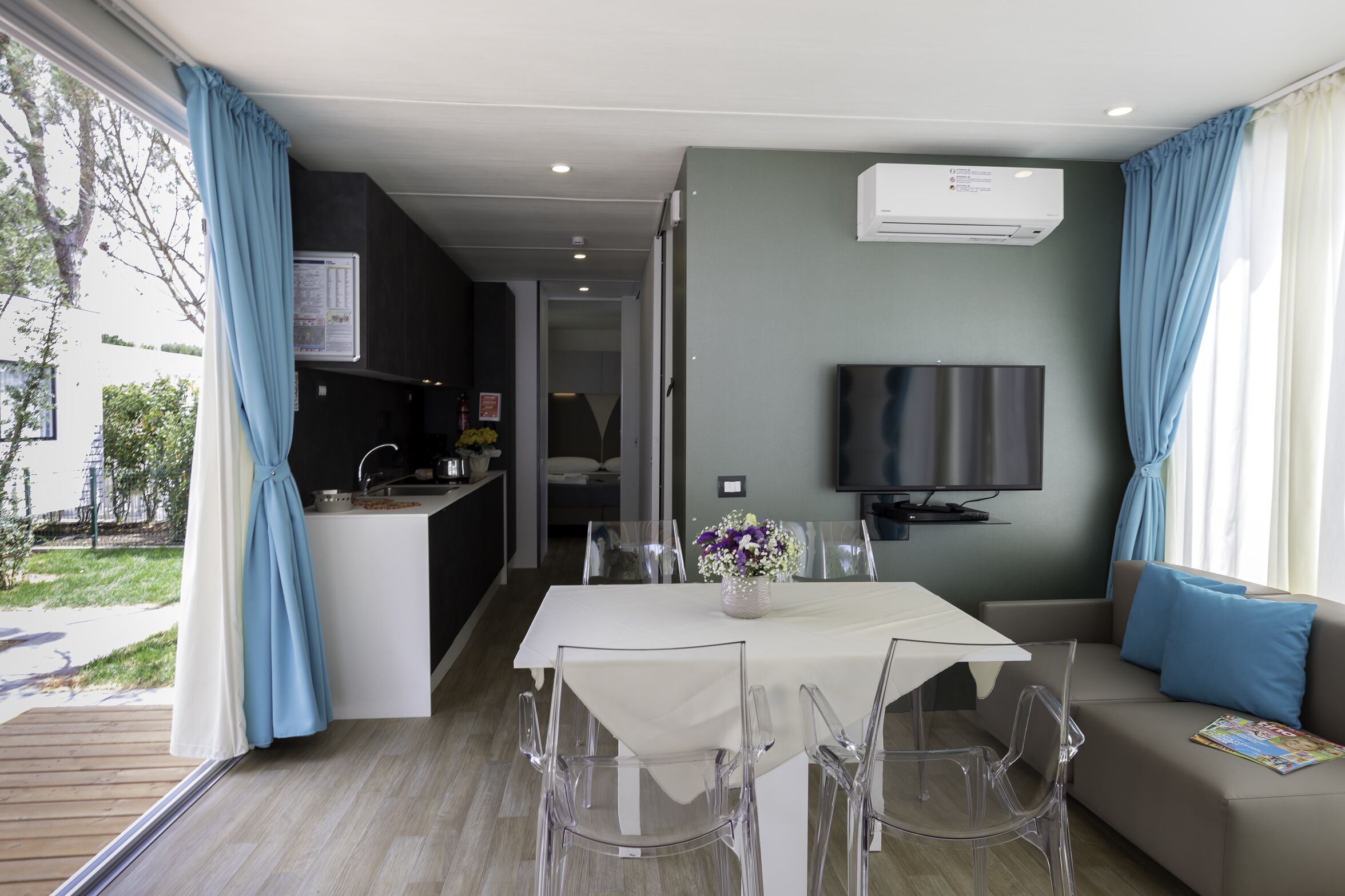 Un salon moderne comprenant un coin repas, un téléviseur à écran plat fixé au mur et une grande fenêtre avec des rideaux.