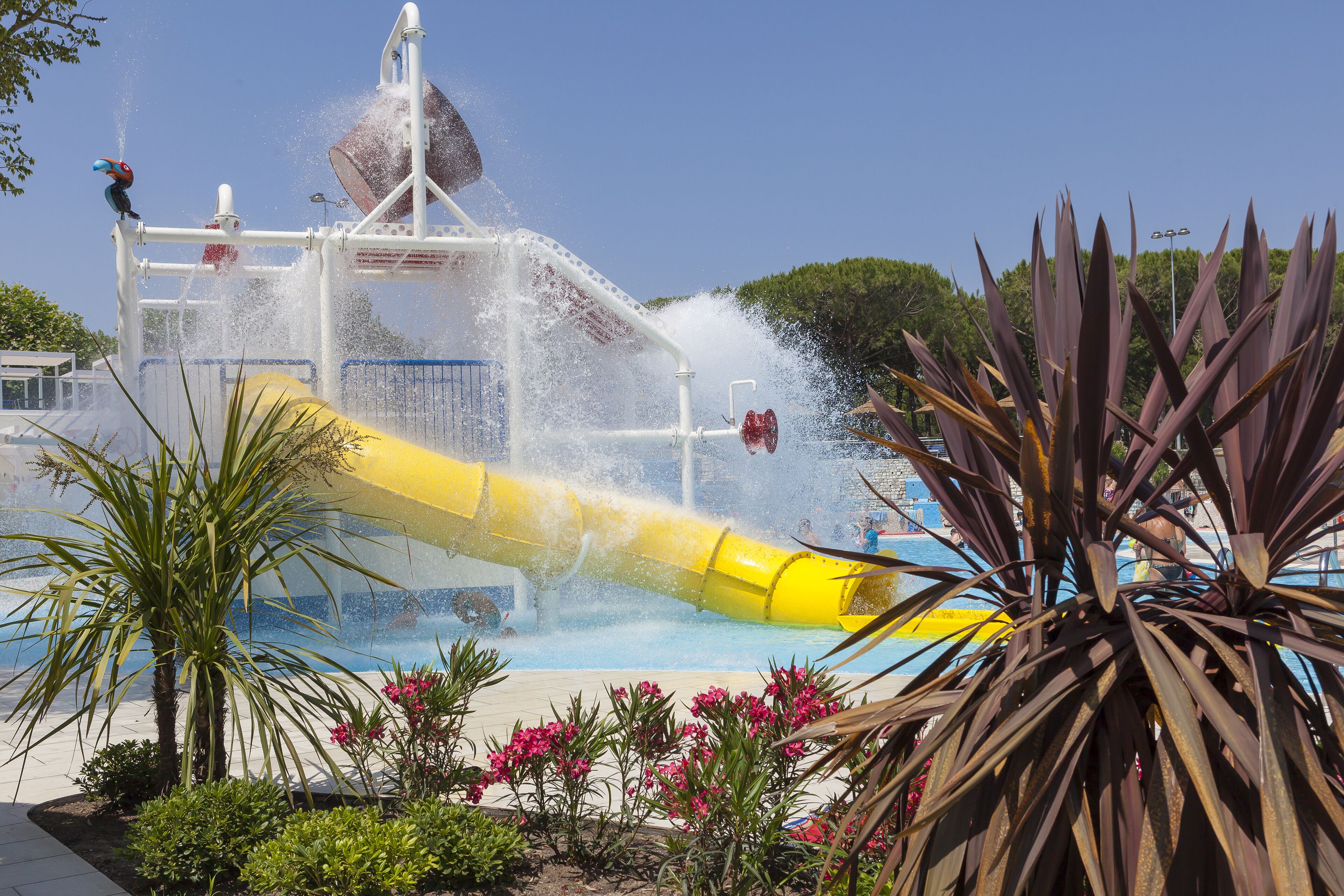 Een waterpark met een gele glijbaan en een fontein.