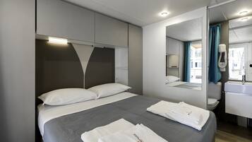 A modern hotel room with a large bed, a built-in wardrobe, a bathroom with a mirror, and a view of the outside.