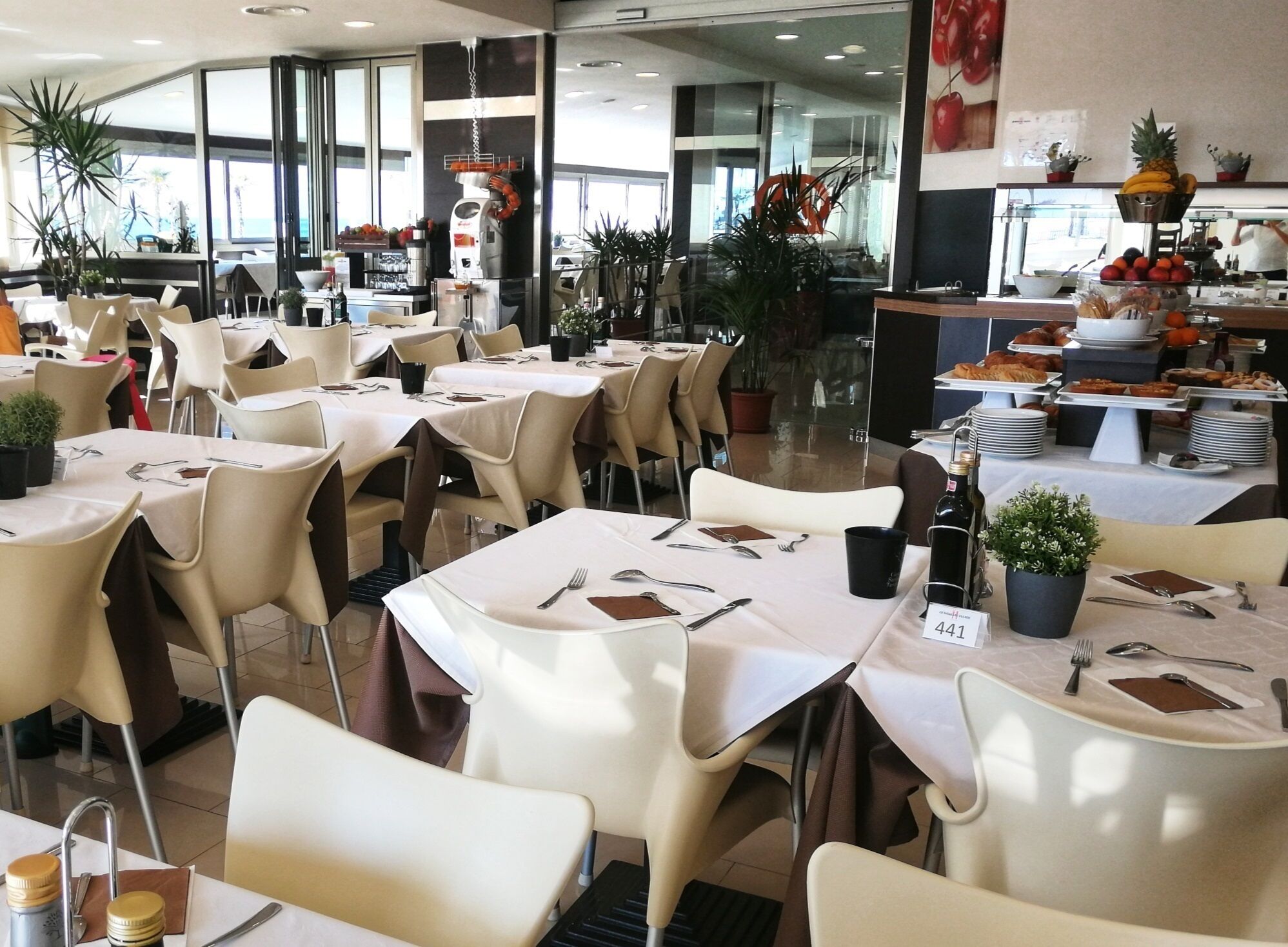 A spacious dining area with multiple tables and chairs, some with potted plants.