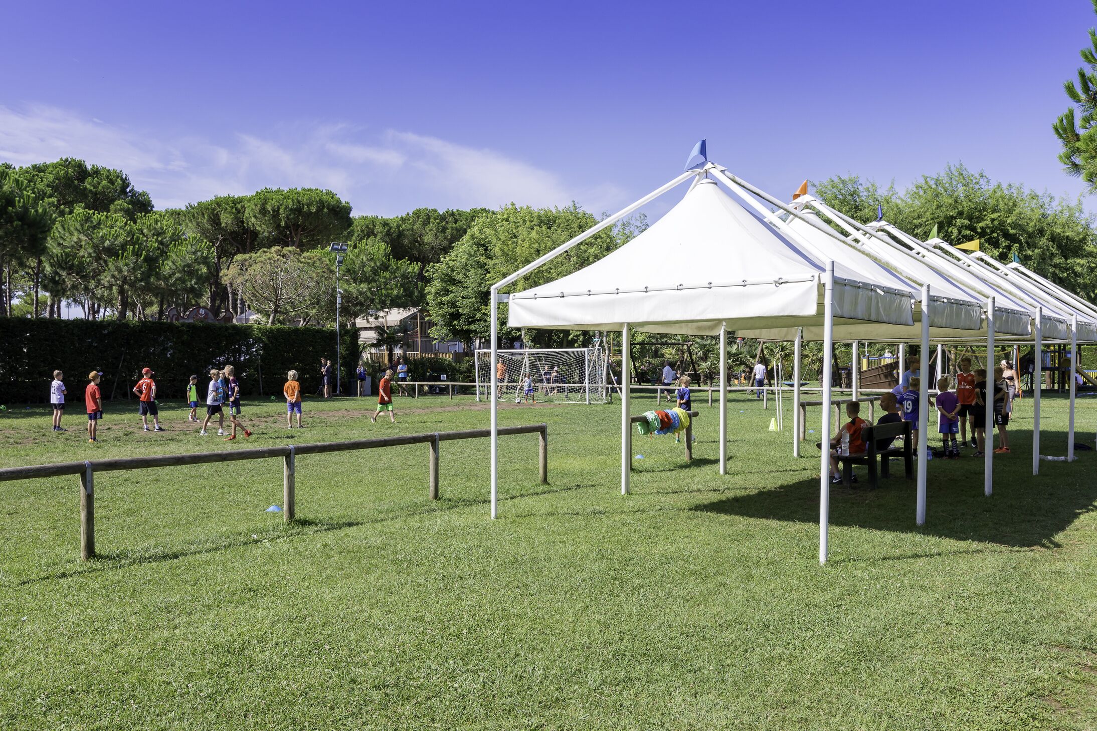 A grassy field with a white tent structure, a soccer goal, and a few people.