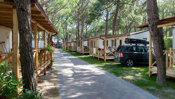 Une rangée de maisons mobiles en bois, avec des voitures garées devant, le tout entouré d’arbres.