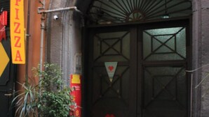 A building with a large arched entrance, a 'PIZZA' sign, and two potted plants in front. - Terrazza Partenopea (Naples)