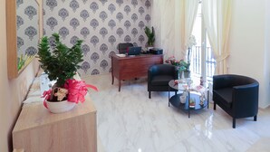 A modern living room with a wooden desk, two black armchairs, a glass coffee table, and a potted plant with a pink ribbon. - Terrazza Partenopea (Naples)