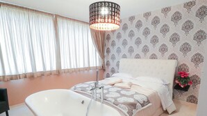 A bedroom with a large bathtub, a bed with a white headboard, and a patterned wallpaper. - Terrazza Partenopea (Naples)