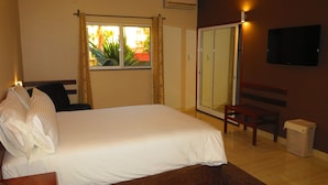 A hotel room with a bed, a desk, a chair, a TV, a wardrobe, and a window with curtains. - Hotel Castelo Branco (Chimoio)