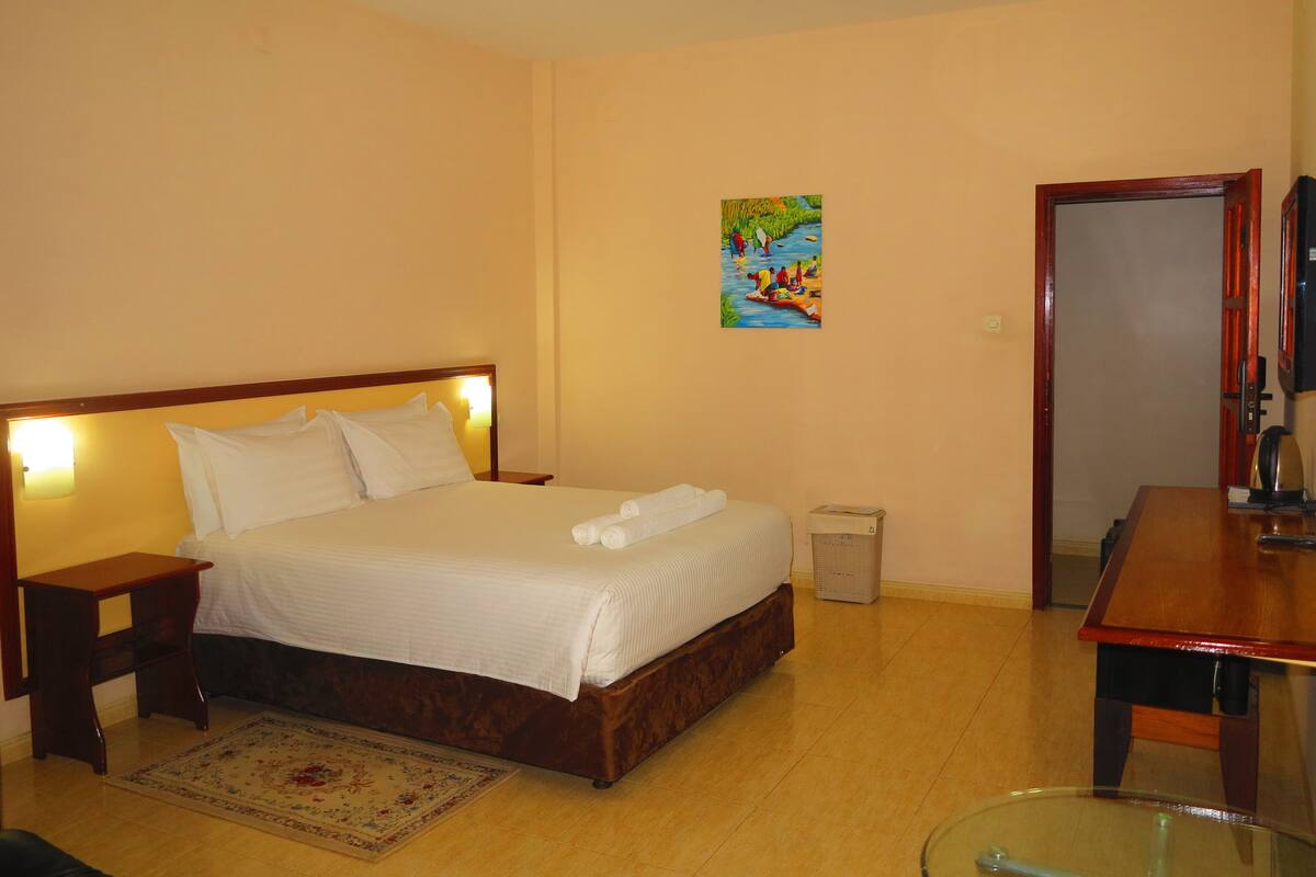A hotel room with a bed, bedside tables, a small trash bin, a wooden desk, and a television.