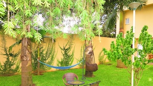 A patio with a table and chairs, surrounded by green grass and trees. - Hotel Castelo Branco (Chimoio)