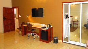 A hotel room with a wooden desk, a chair, a television mounted on the wall, and a sliding glass door leading to a balcony. - Hotel Castelo Branco (Chimoio)