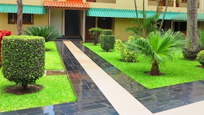 A courtyard with a tiled pathway, neatly trimmed hedges, and palm trees. - Hotel Castelo Branco (Chimoio)