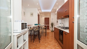 Une cuisine de taille réduite avec un coin repas, des meubles blancs et un sol carrelé.