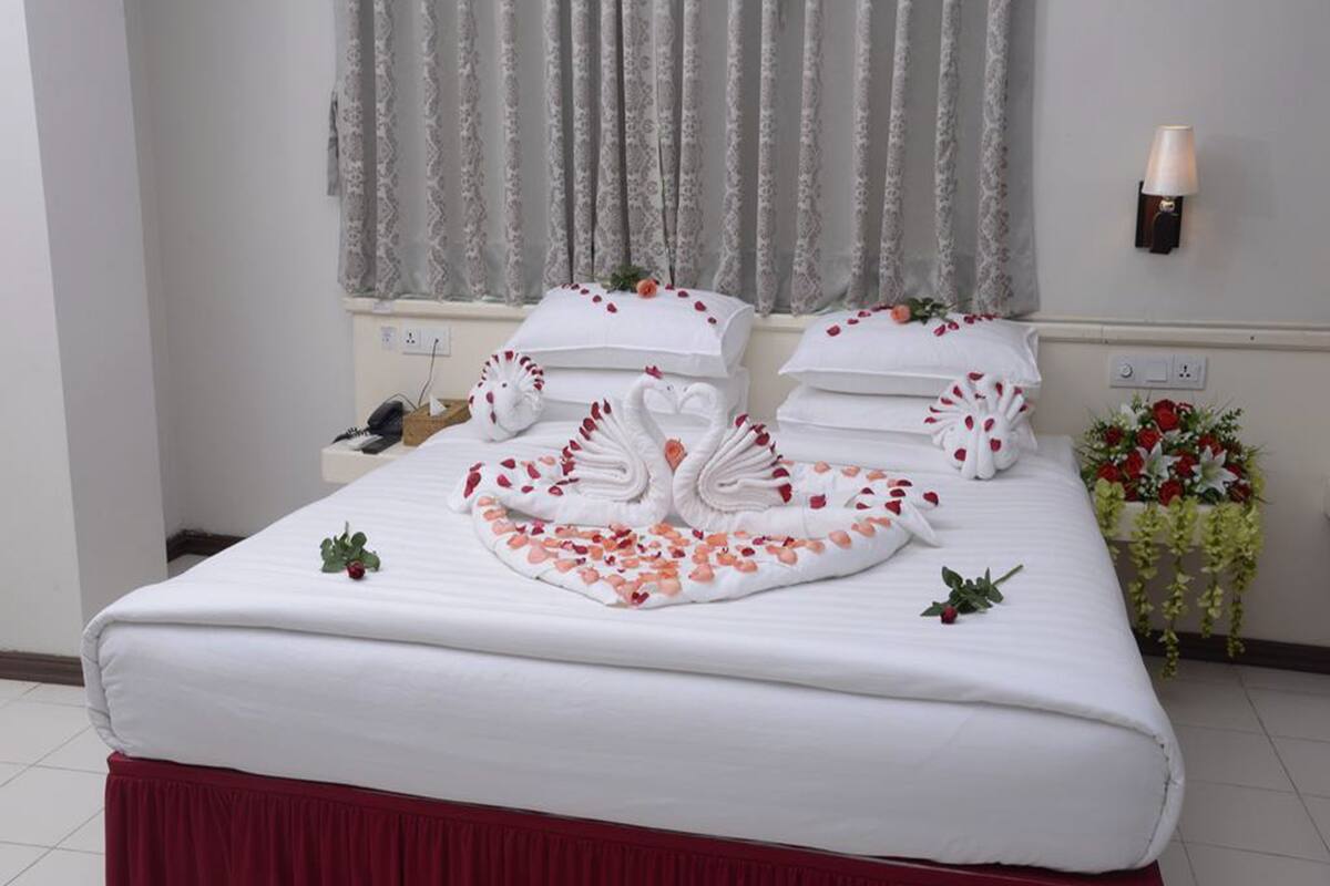 A neatly made bed with a swan towel arrangement, a red skirt, and a vase of flowers.