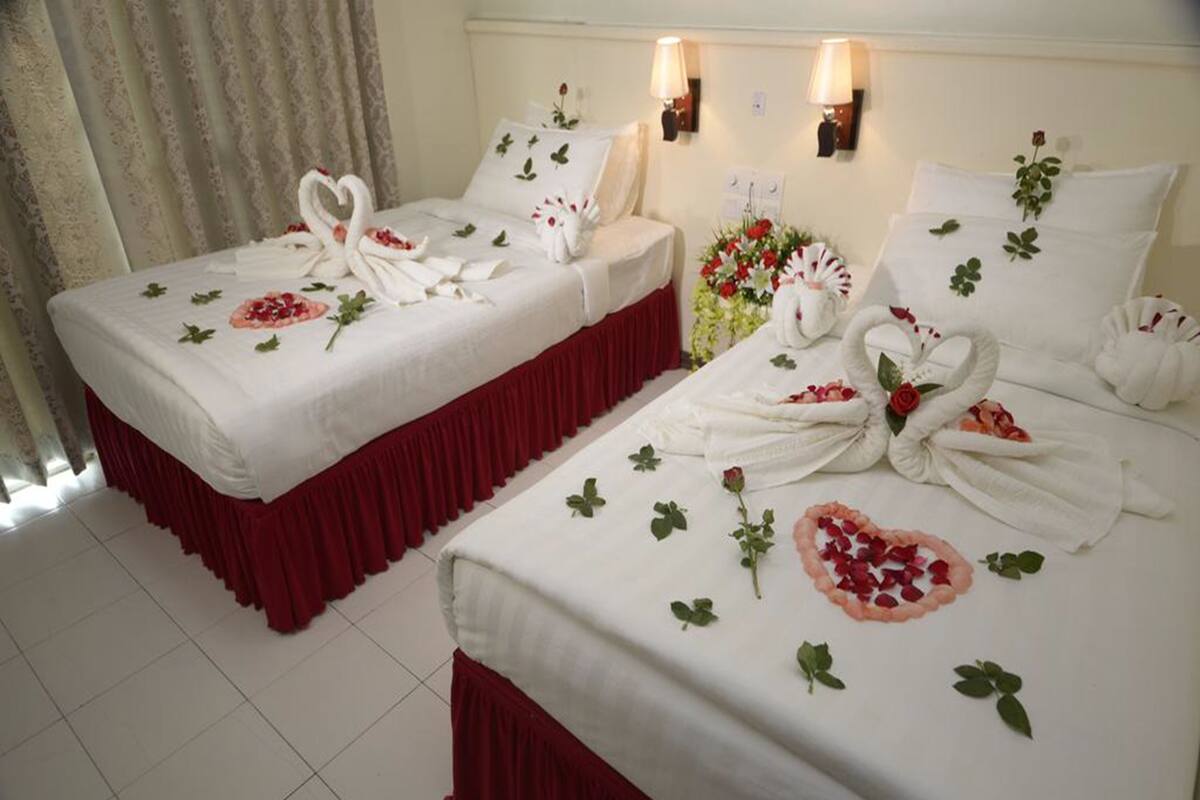 Two hotel beds with white linens, red skirts, and decorative swans made from towels.