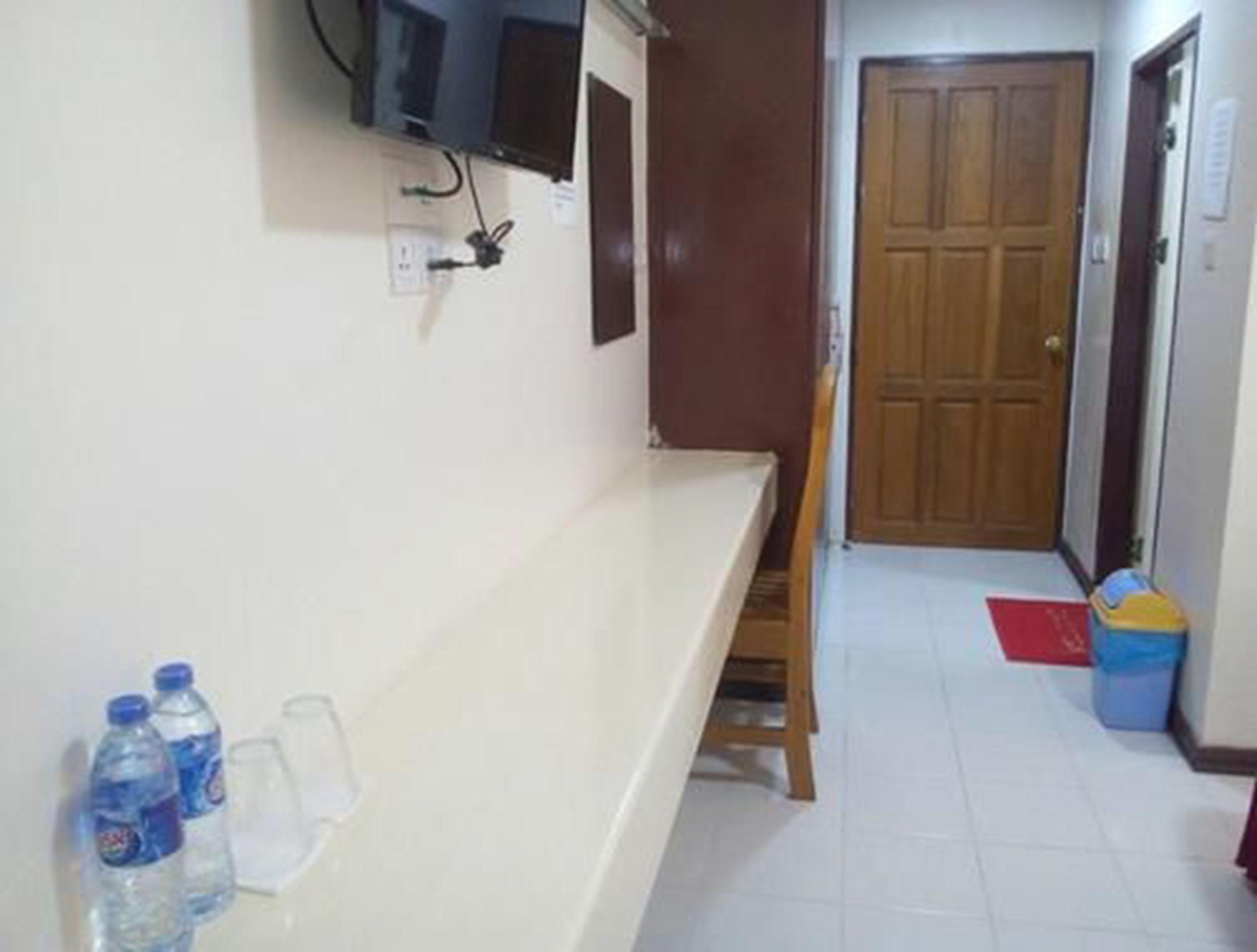 A room with a white counter, a television mounted on the wall, a wooden door, and a trash bin.