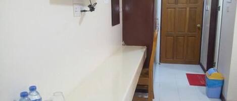 A room with a white counter, a television mounted on the wall, a wooden door, and a trash bin.